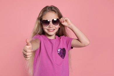 Photo of Girl in stylish sunglasses showing thumb up on pink background