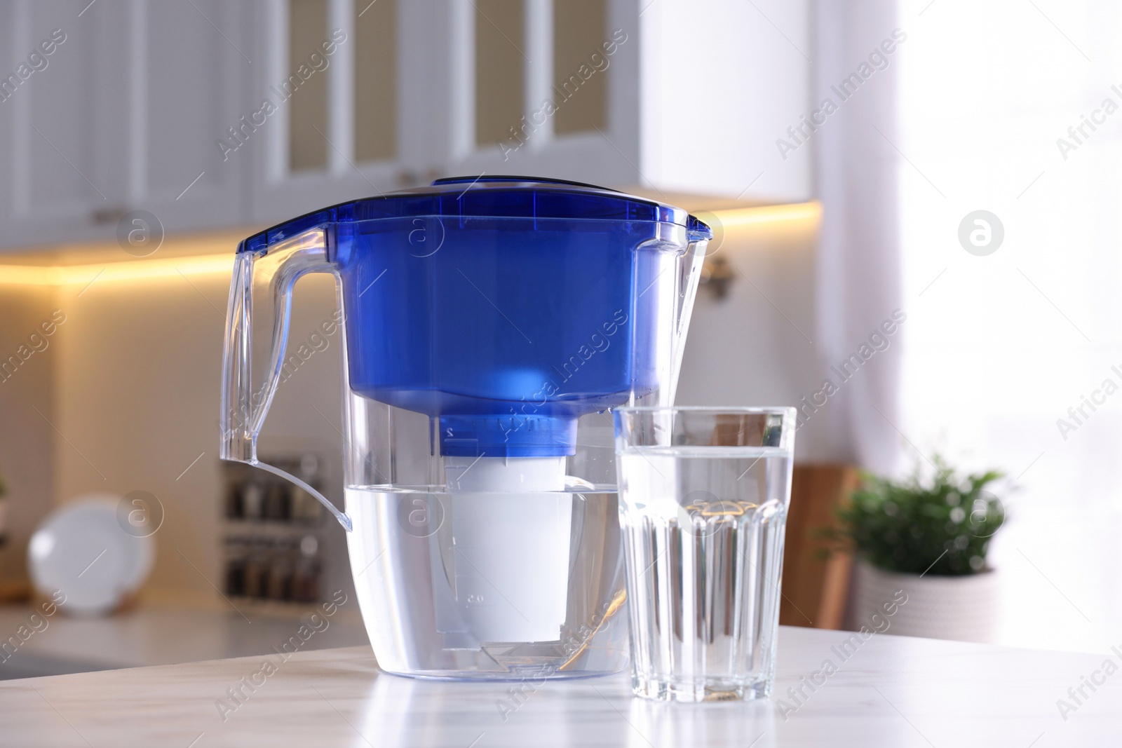 Photo of Water filter jug and glass on white marble table in kitchen, closeup