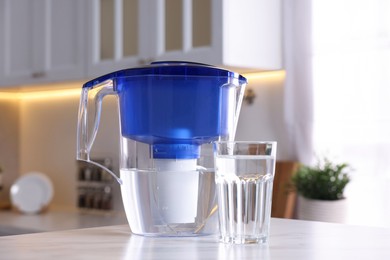 Water filter jug and glass on white marble table in kitchen, closeup