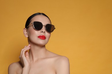 Photo of Attractive woman in fashionable sunglasses against orange background. Space for text