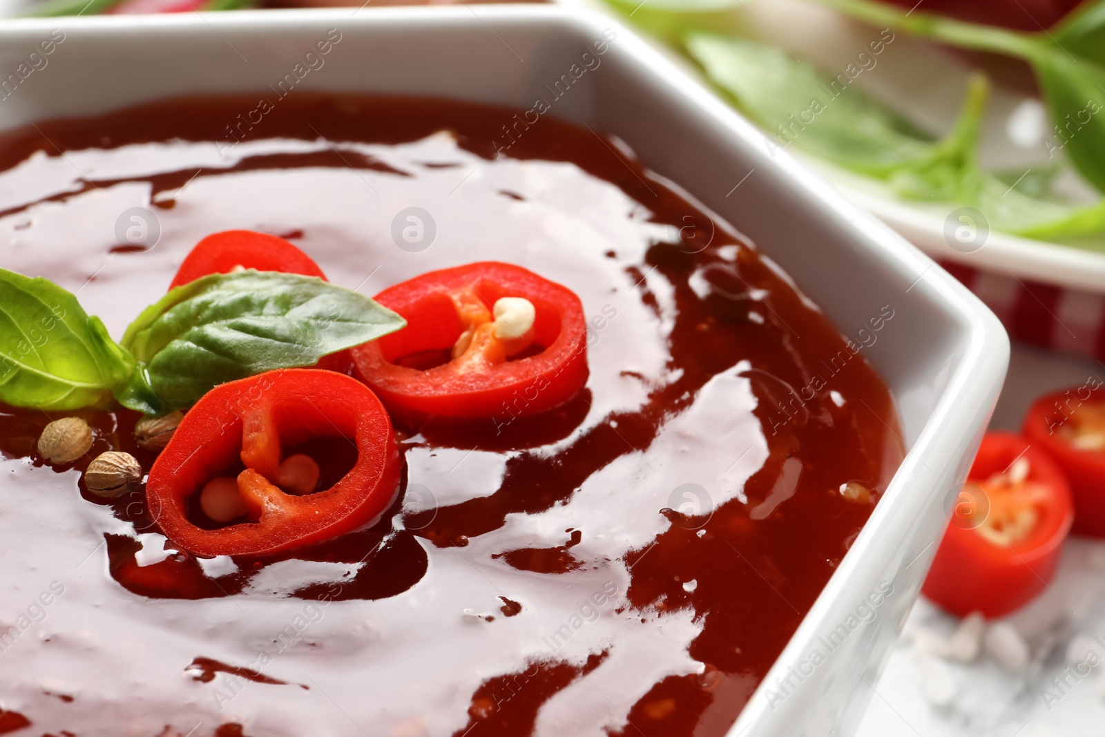 Photo of Spicy chili sauce with basil in bowl on table, closeup