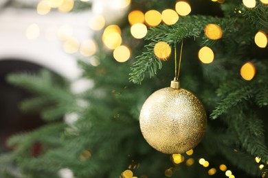 Photo of Christmas ball hanging on fir tree branch indoors, closeup. Space for text