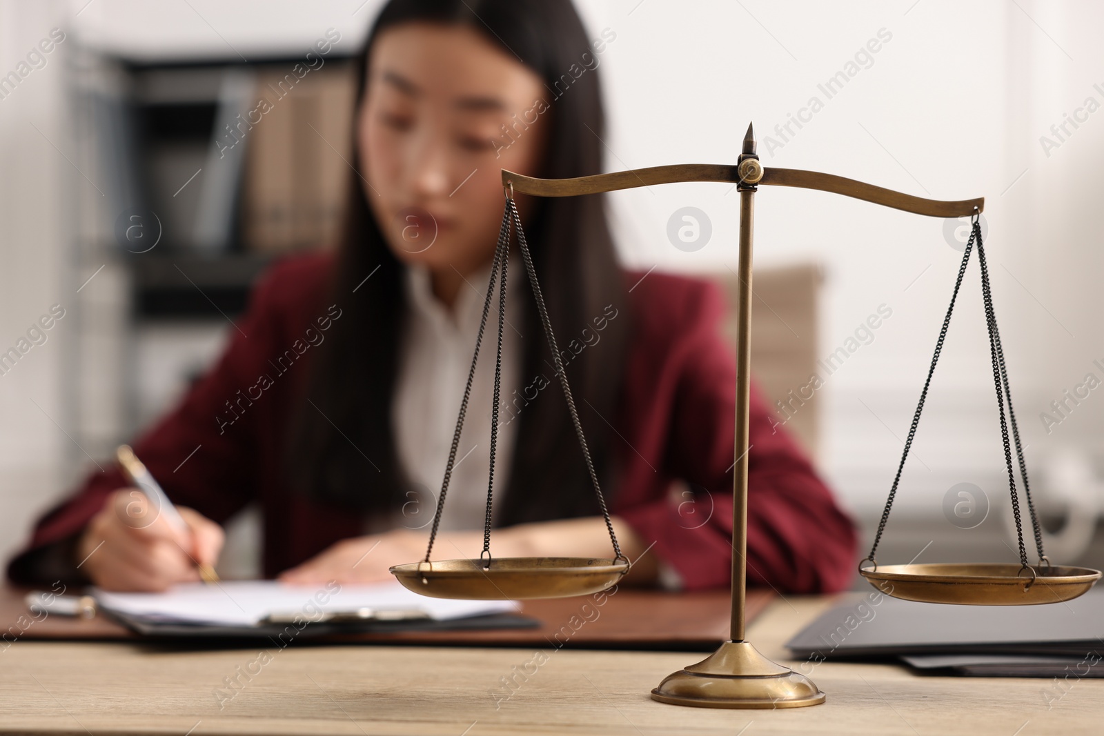 Photo of Notary signing document at wooden table in office, focus on scales