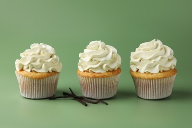 Photo of Tasty cupcakes with cream and vanilla pods on green background