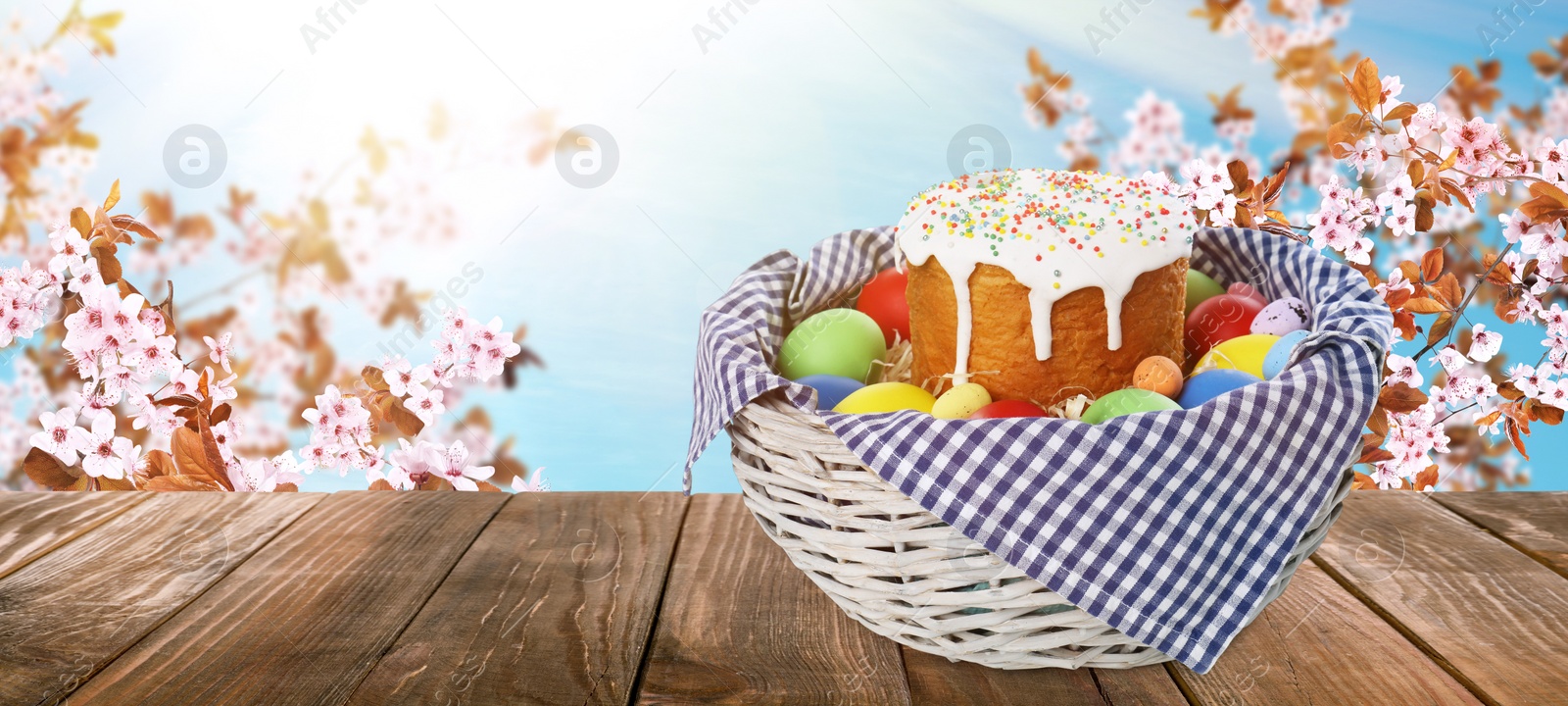 Image of Basket with traditional Easter cake and eggs on wooden table outdoors, space for text. Banner design