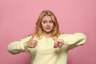 Photo of Conflicted young woman showing thumbs up and down gestures on pink background