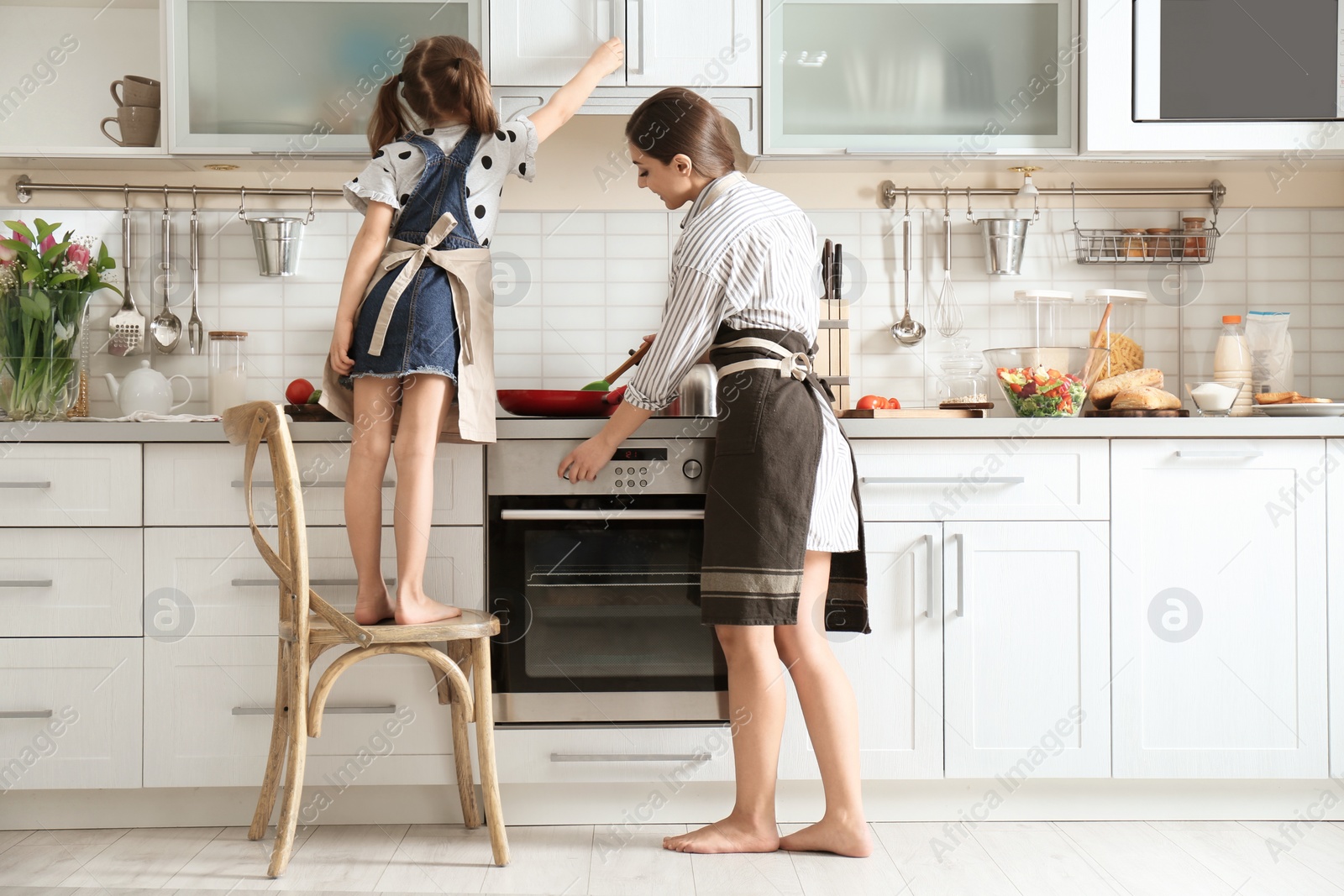 Photo of Young nanny with cute little girl cooking together in kitchen