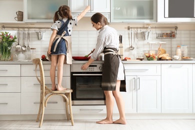 Young nanny with cute little girl cooking together in kitchen