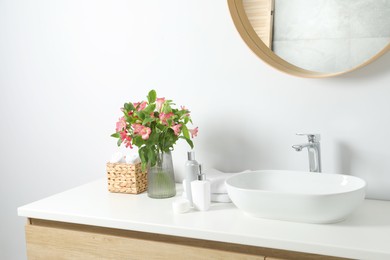 Vase with beautiful Alstroemeria flowers and toiletries near sink in bathroom