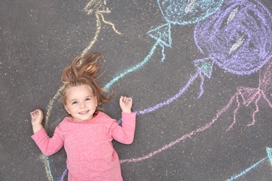 Little child lying near chalk drawing of balloons on asphalt, top view