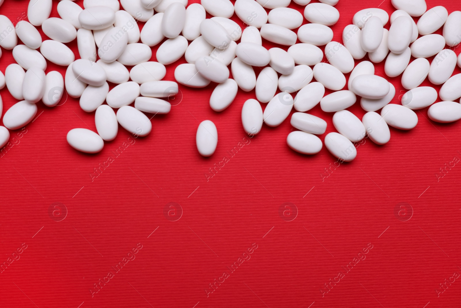 Photo of Many white dragee candies on red background, flat lay. Space for text