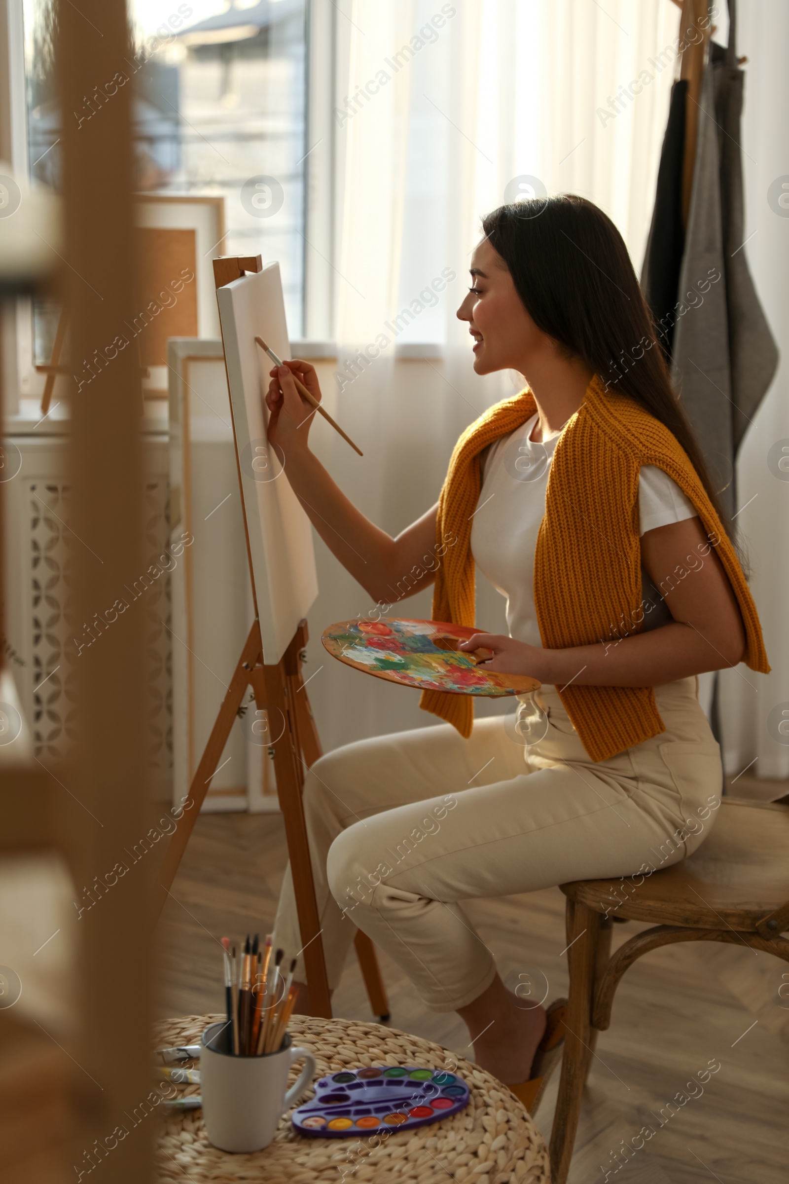 Photo of Beautiful young woman drawing on easel at home