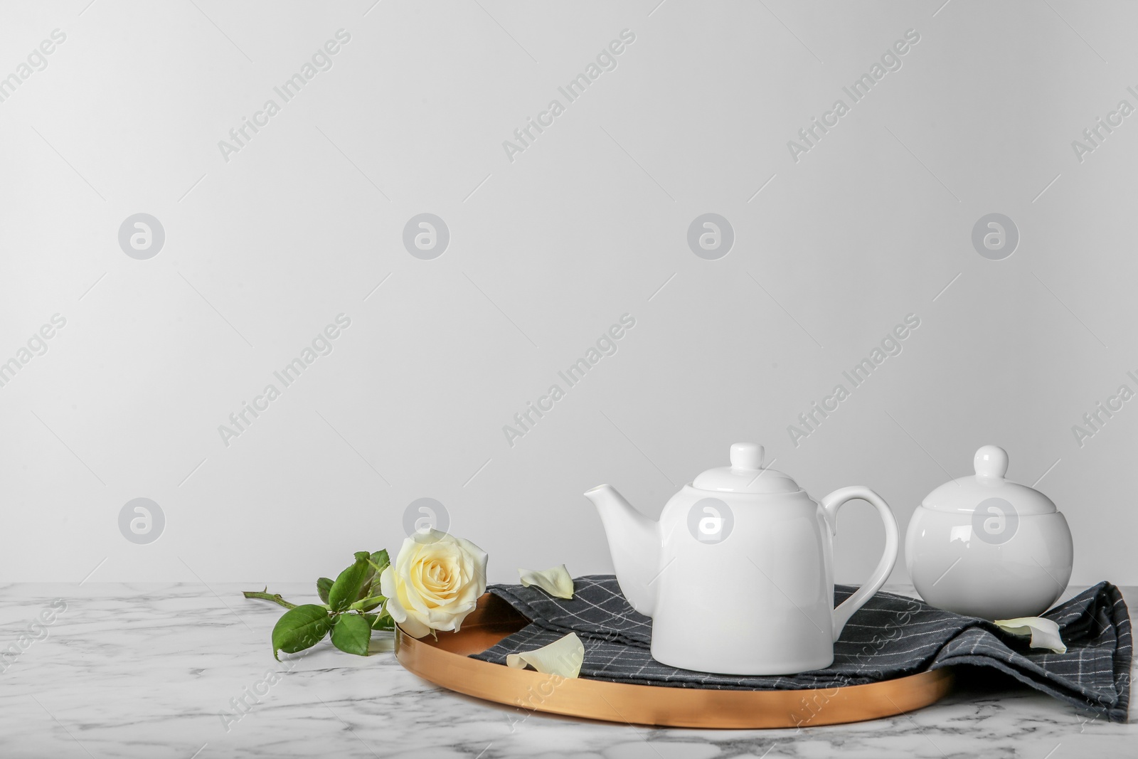 Photo of Tray with teapot and rose on table against light background