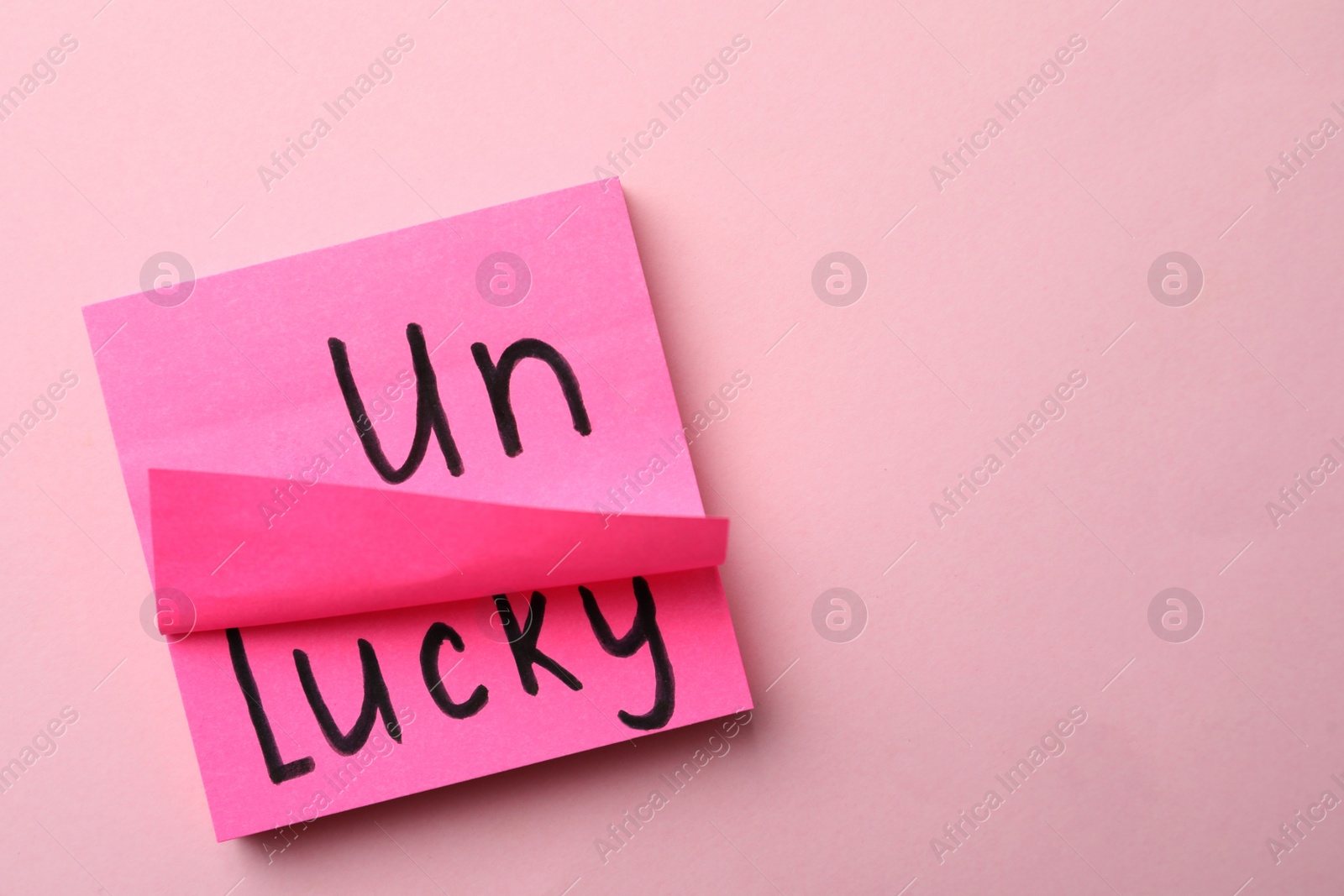 Photo of Notes with word UNLUCKY on pink background, top view. Space for text