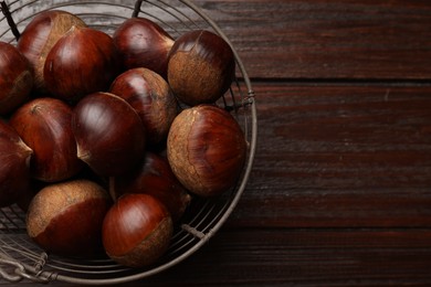 Photo of Sweet fresh edible chestnuts in metal basket on wooden table, top view. Space for text