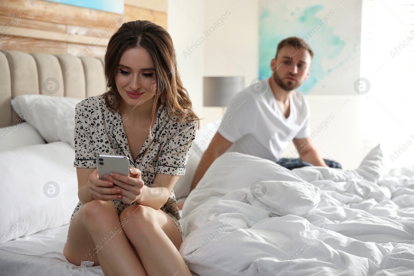 Photo of Young man peering into girlfriend's smartphone at home. Jealousy in relationship