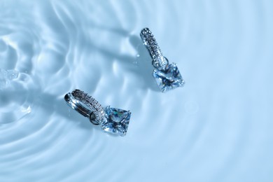 Luxury jewelry. Elegant earrings in water on light blue background