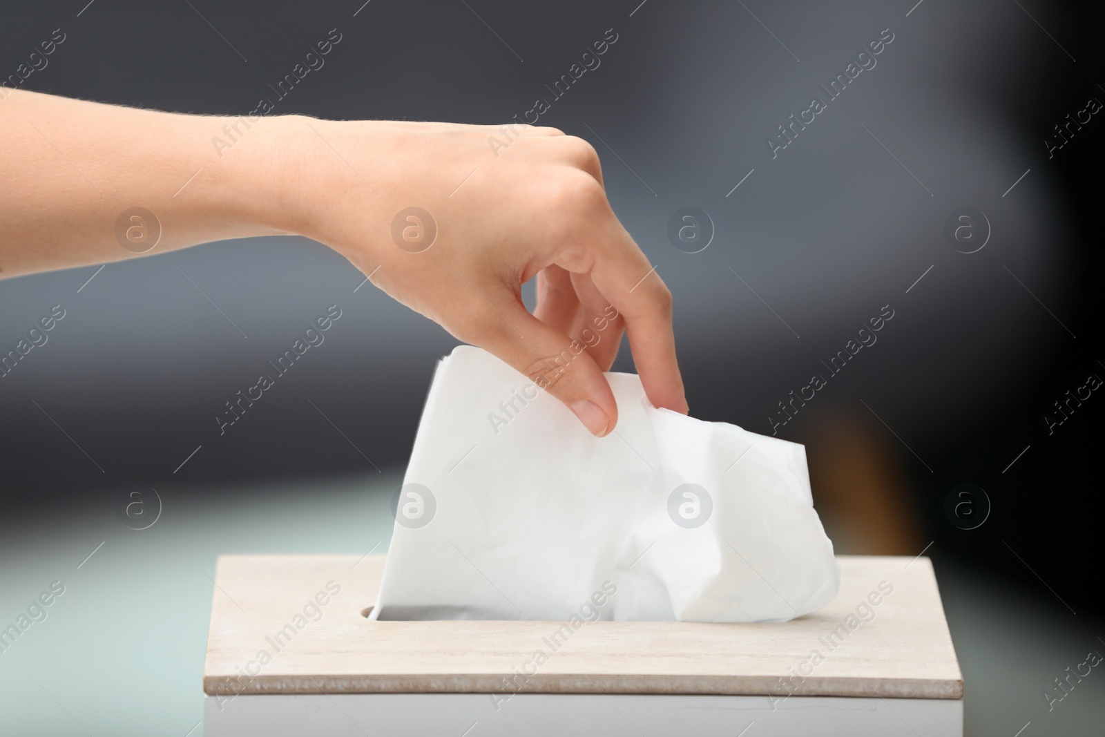 Photo of Woman taking paper tissue from holder on blurred background, closeup