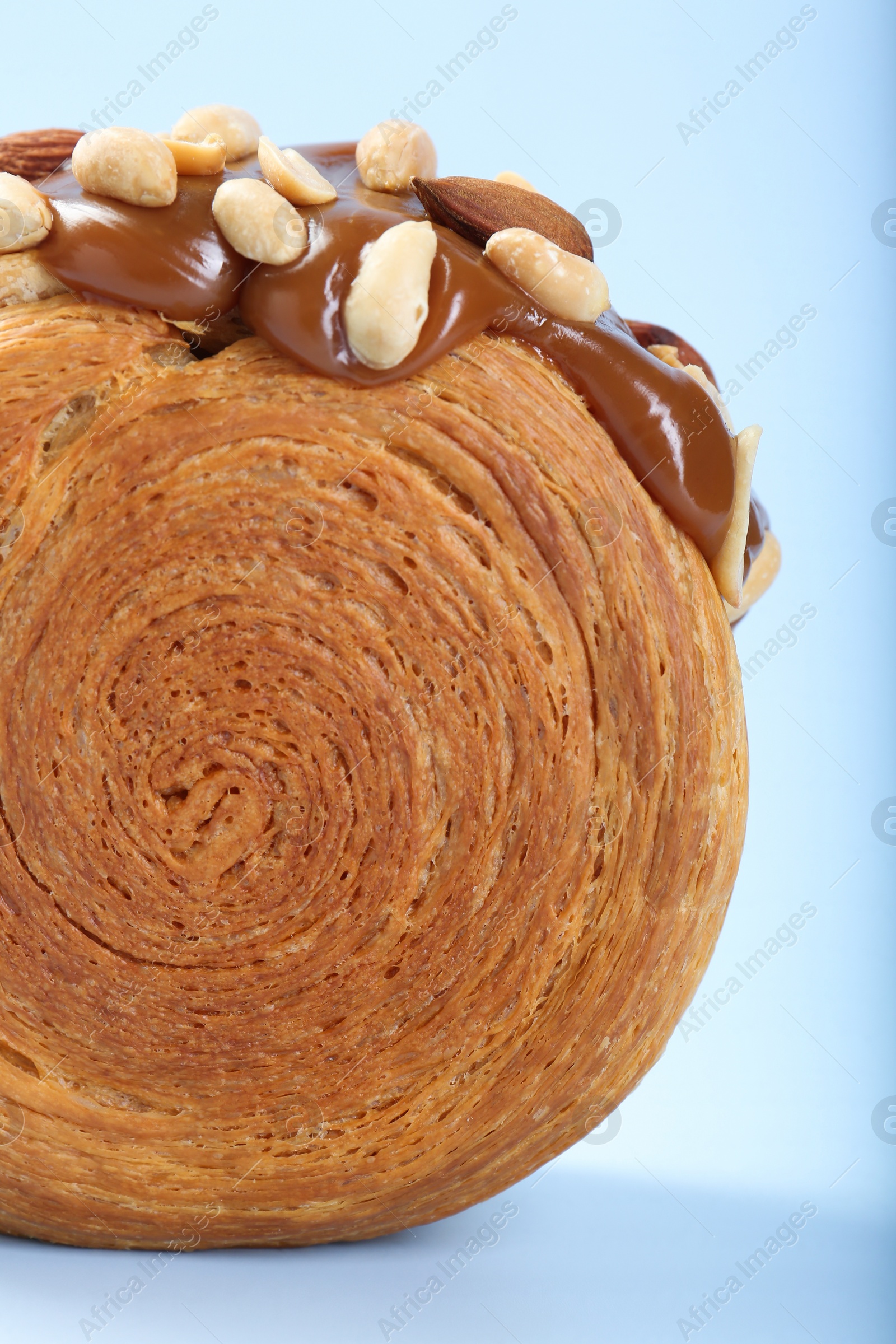 Photo of One supreme croissant with chocolate paste and nuts on light blue background, closeup. Tasty puff pastry