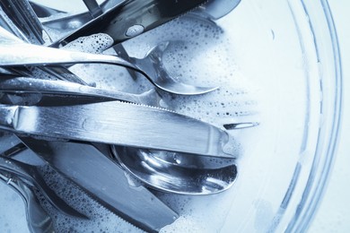 Photo of Glass bowl with silverware in foam, top view. Toned in blue
