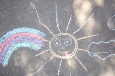 Photo of Child's chalk drawing of sun and rainbow on asphalt, top view