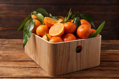 Photo of Fresh tangerines with green leaves in crate on wooden table