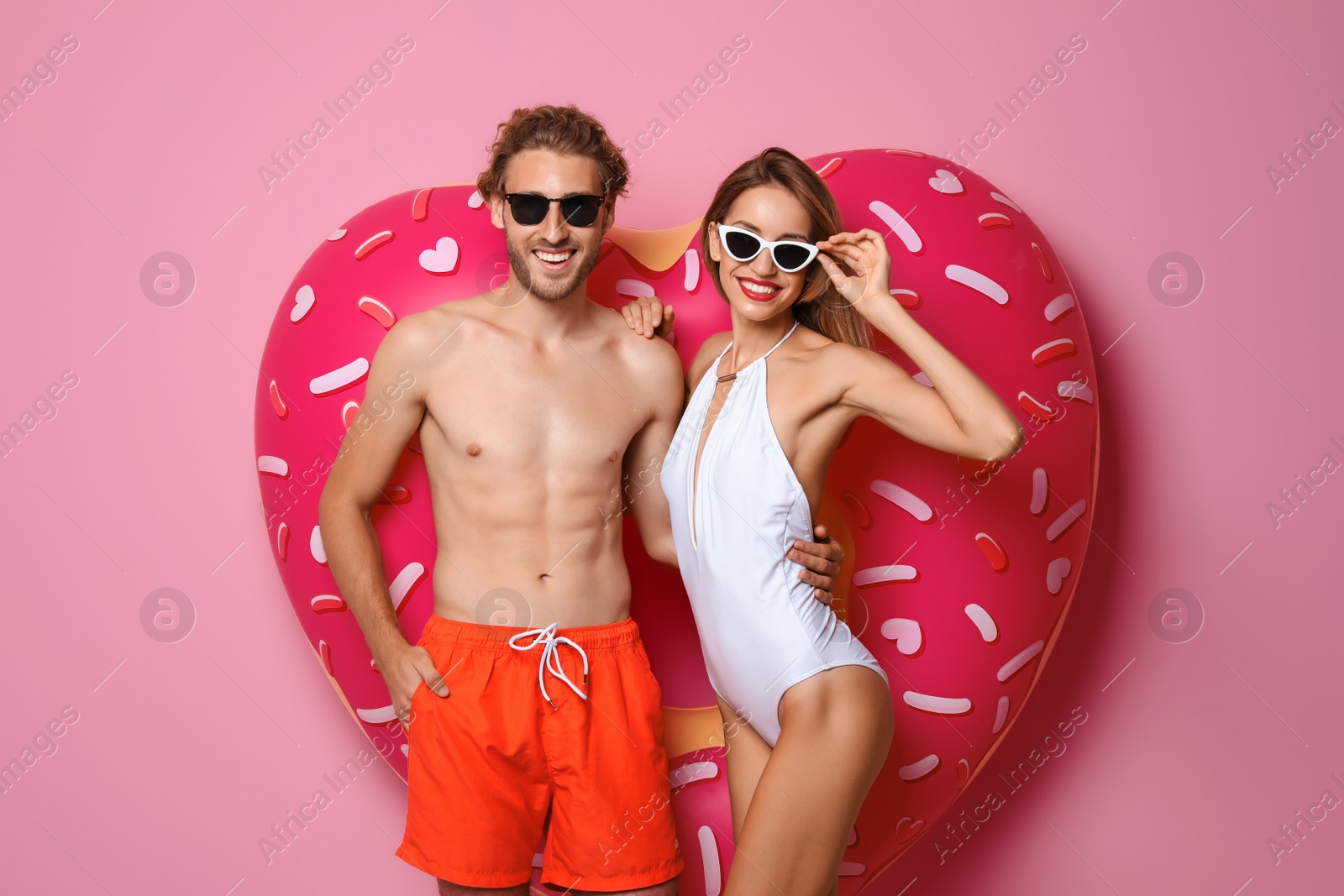 Photo of Happy young couple in beachwear with inflatable ring on color background