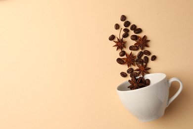 Coffee beans and anise stars falling into cup on beige background, flat lay. Space for text