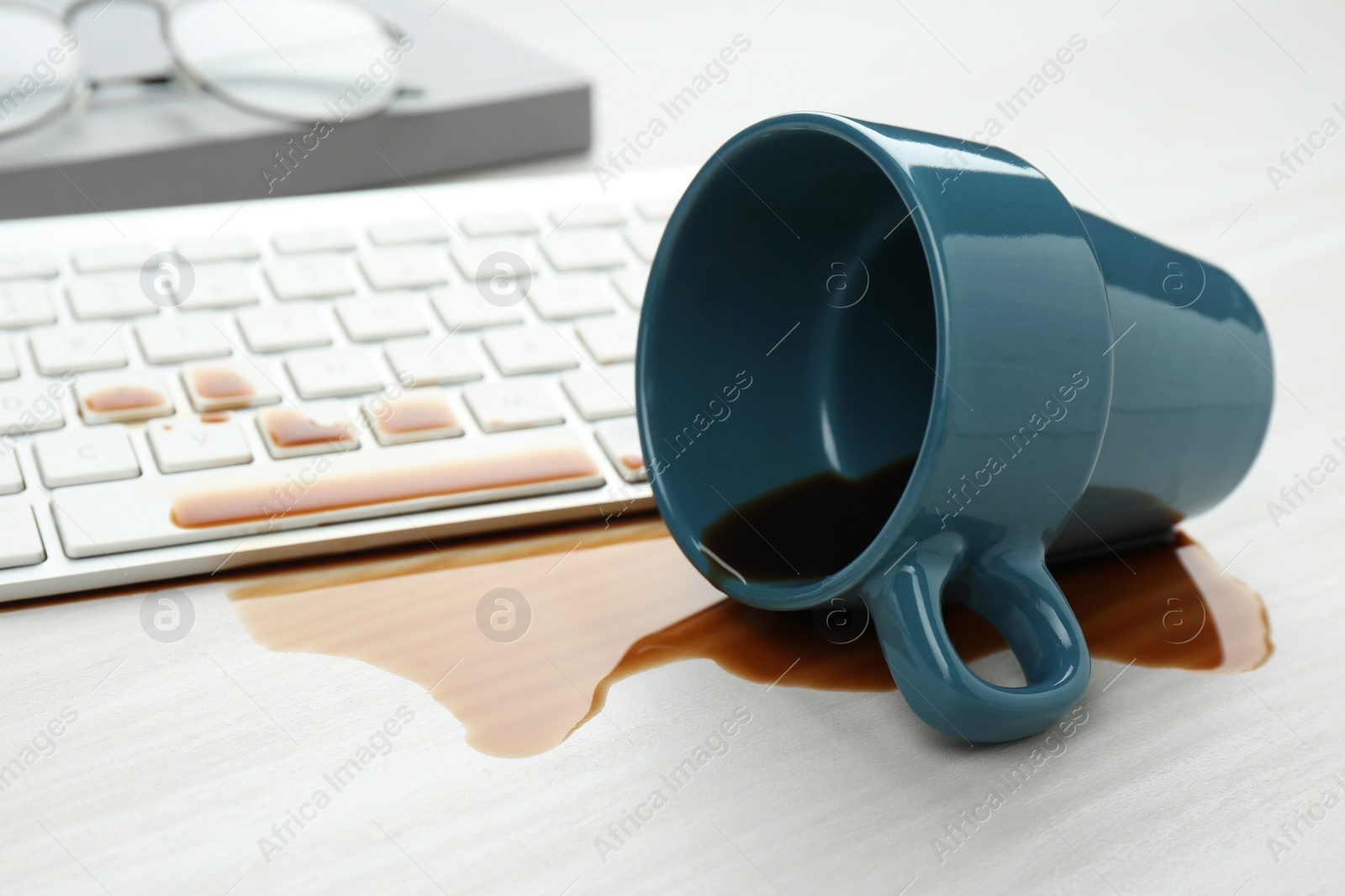 Photo of Cup of coffee spilled over computer keyboard on white wooden table