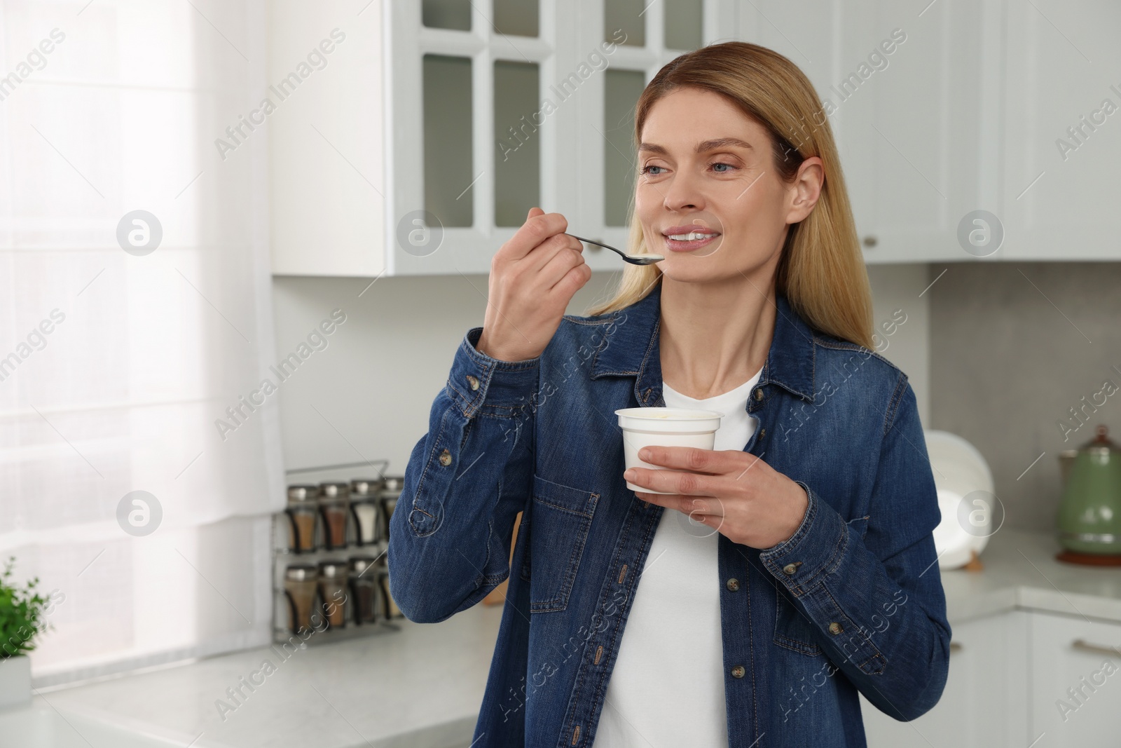 Photo of Woman eating tasty yogurt with spoon in kitchen. Space for text