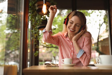 Photo of Young woman with headphones listening to music in cafe