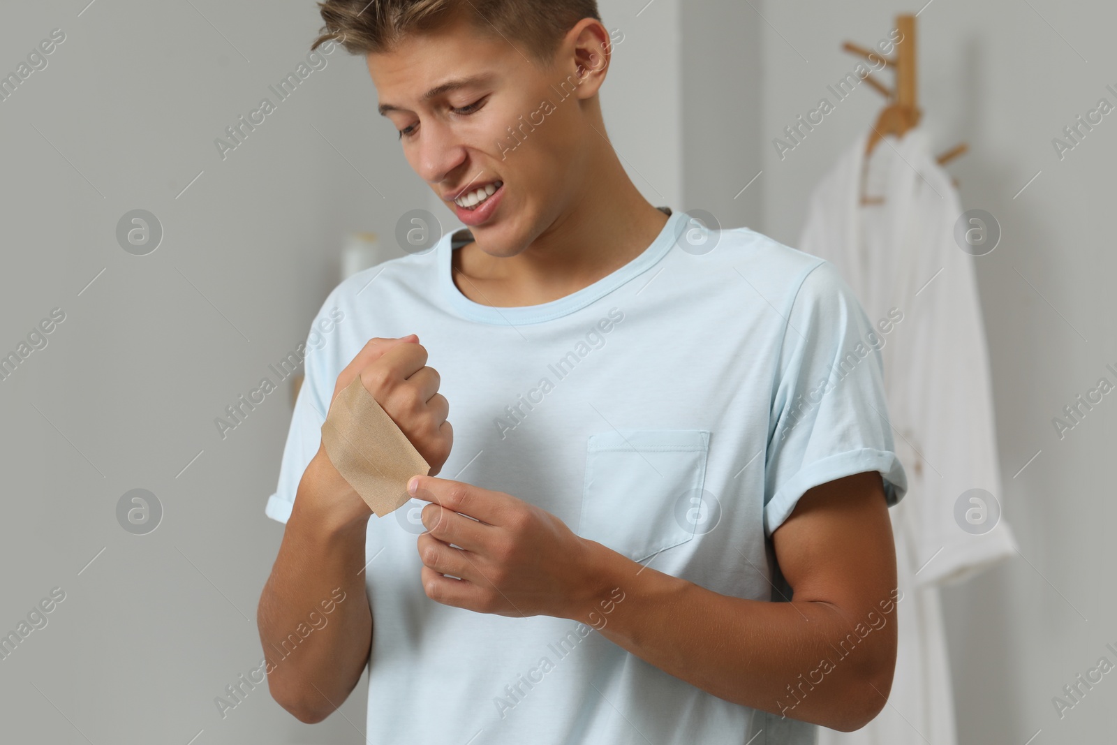 Photo of Handsome man putting sticking plaster onto hand indoors