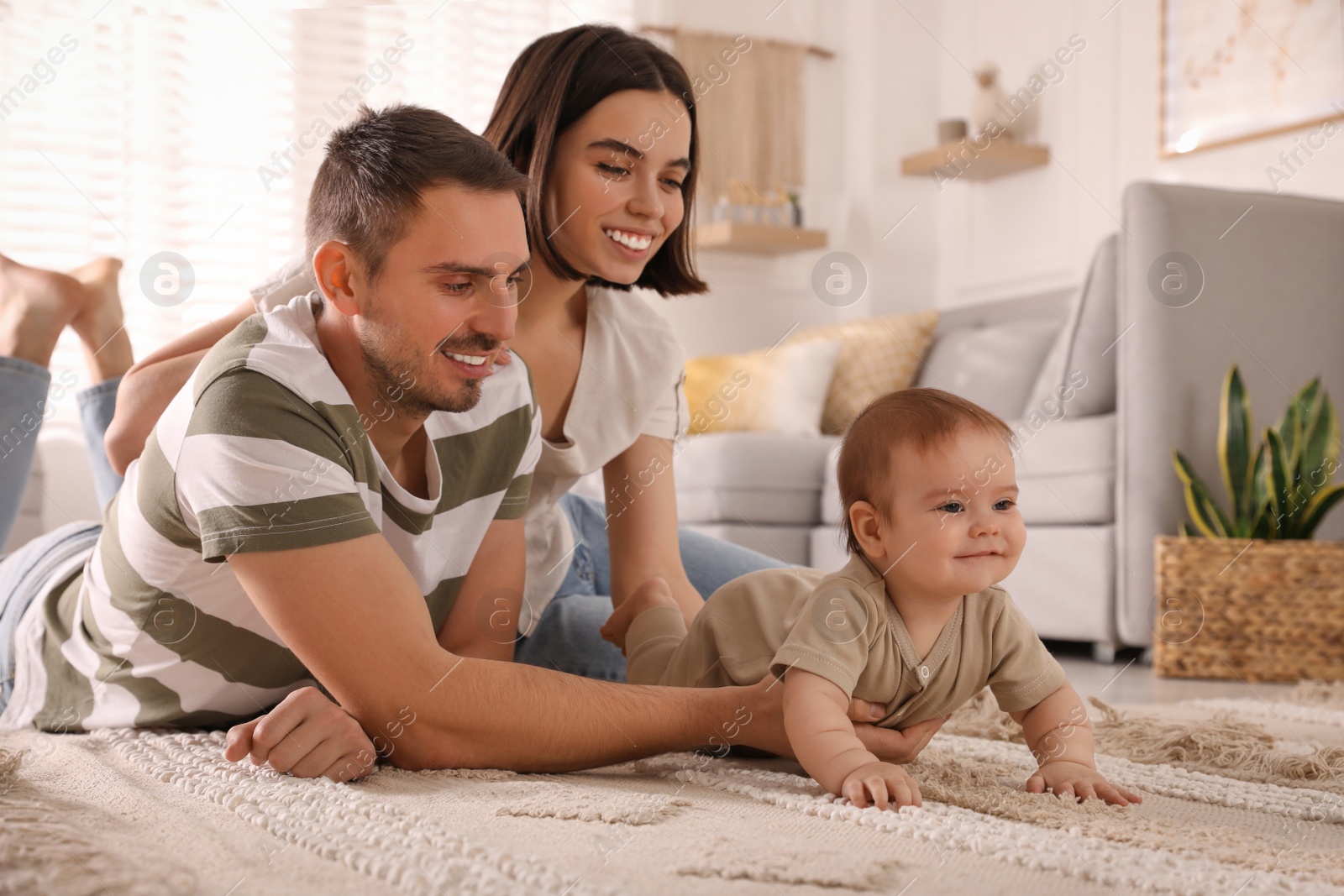 Photo of Happy parents helping their cute baby to crawl on floor at home