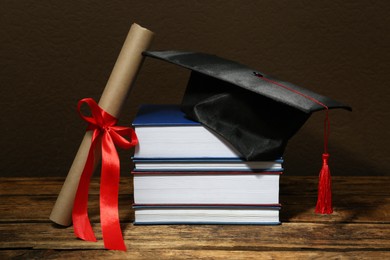 Photo of Graduation hat, books and diploma on wooden table against brown background