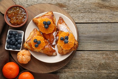 Photo of Fresh tasty puff pastry with sugar powder, jam, tangerines and blueberries on wooden table, flat lay. Space for text