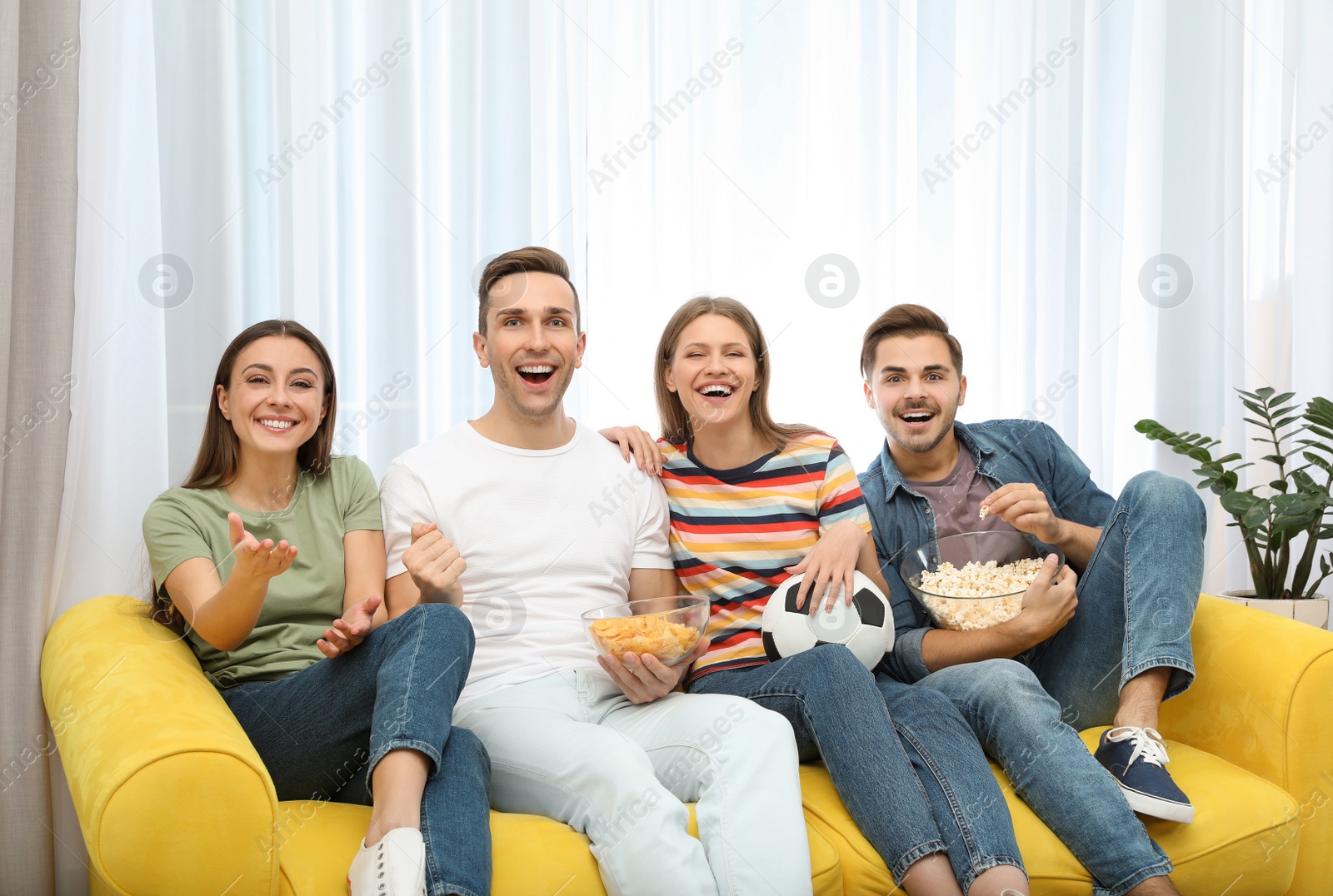 Photo of Group of people with snacks and ball watching soccer match on TV at home