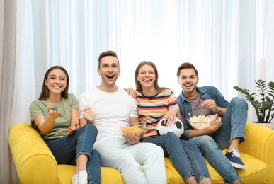 Group of people with snacks and ball watching soccer match on TV at home