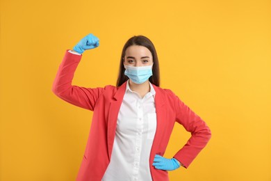 Businesswoman with protective mask and gloves showing muscles on yellow background. Strong immunity concept