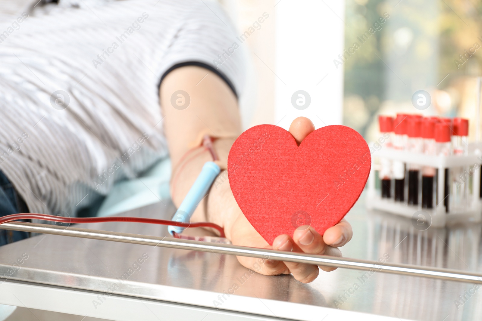 Photo of Man holding heart while making blood donation at hospital, closeup