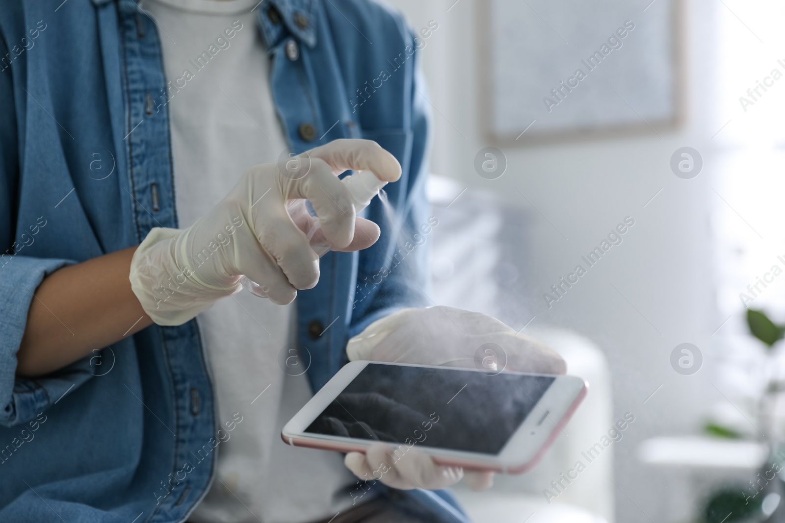 Photo of Woman applying antibacterial spray onto smartphone indoors, closeup