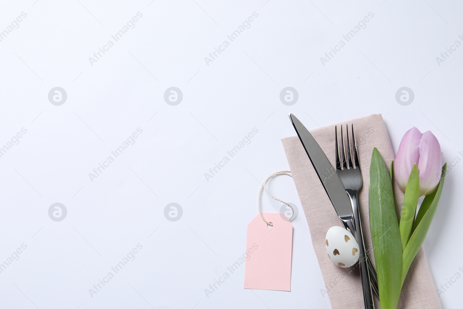 Photo of Cutlery set, Easter egg and tulip on white background, top view with space for text. Festive table setting