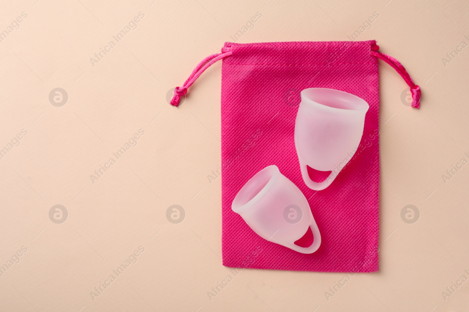 Photo of Menstrual cups with cotton bag on beige background, top view. Space for text