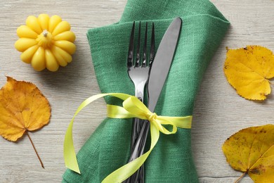 Photo of Thanksgiving table setting. Cutlery, napkin, autumn leaves and pumpkin shaped candle on light wooden background, flat lay