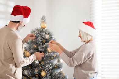Happy couple in Santa hats decorating Christmas tree at home