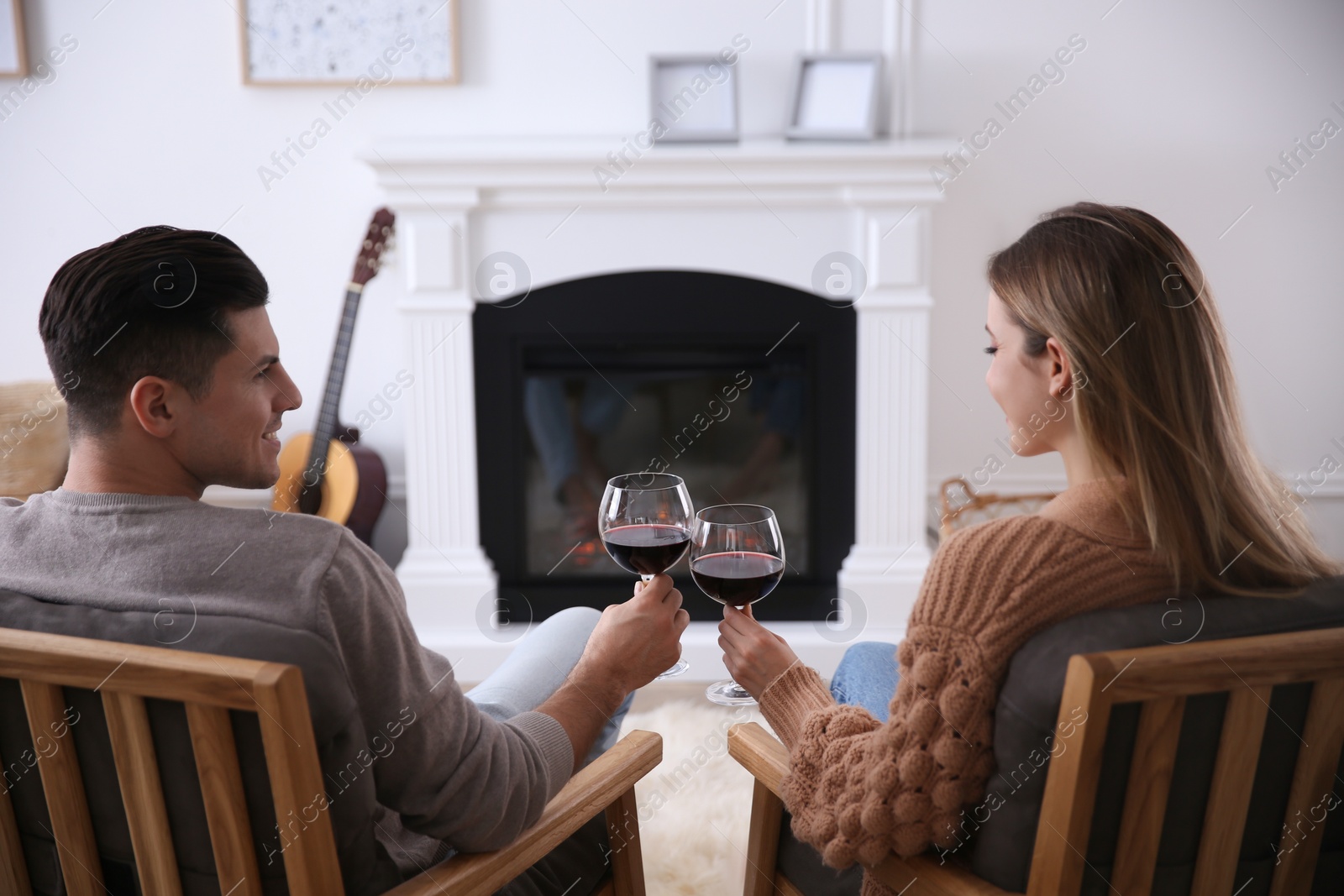 Photo of Happy couple toasting with glasses of wine near fireplace at home