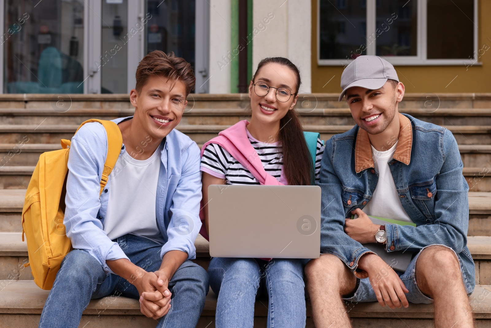 Photo of Happy young students studying together with laptop on steps outdoors