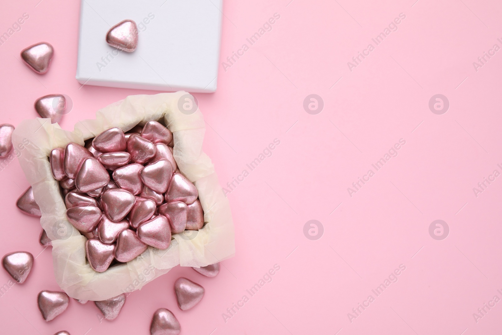 Photo of Box and delicious heart shaped candies on pink background, flat lay. Space for text