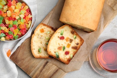 Photo of Delicious cake with candied fruits and tea on light grey table, flat lay