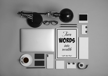 Card with phrase Turn Words Into Wealth, laptop and stationery on grey table, flat lay