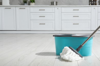 Photo of Mop and bucket on white parquet in kitchen, space for text. Cleaning floor
